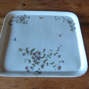 Puede incluir: Una bandeja de servir de cerámica blanca con un diseño floral que presenta flores azules y rosas, hojas verdes y mariposas naranjas.