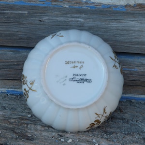 May include: White ceramic bowl with a gold floral design and the text "Decor Main" and "Pillivuyt" on the bottom.
