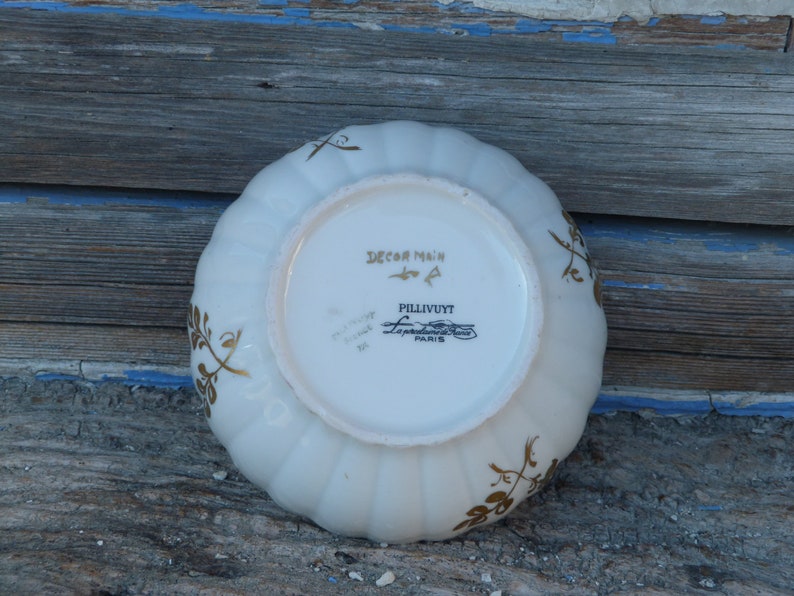 May include: White ceramic bowl with a gold floral design and the text "Decor Main" and "Pillivuyt" on the bottom.