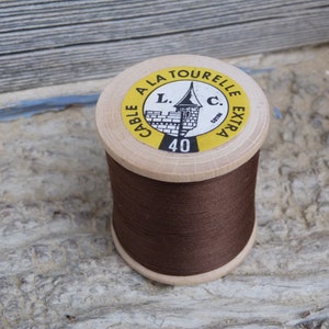 Op de afbeelding: Een spoel bruin garen met het label "Cable a la Tourelle L.C. Extra 40 Cotton" en een kleine afbeelding van een toren.