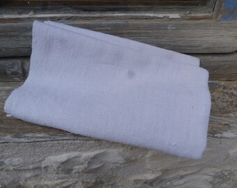 May include: A white linen fabric folded in half, with a slightly textured surface. The fabric is lying on a wooden surface.