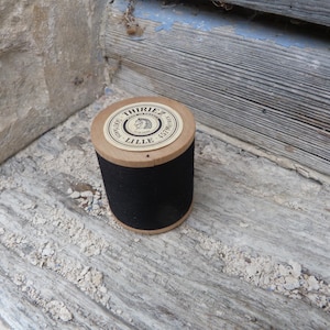 Può includere: Una bobina cilindrica di filo nero con una parte superiore in cartone color marrone chiaro. L'etichetta sulla parte superiore riporta il testo THIRIEZ, MADE IN FRANCE, LILLE, 500 GRAMS e 457 METRES, con un piccolo grafico di una testa di cavallo.