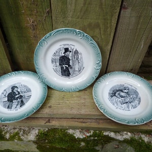 Könnte beinhalten: Drei antike Keramikteller mit grünem Rand und Schwarzweißillustrationen. Die Teller zeigen Szenen von Menschen in Kleidung aus dem 19. Jahrhundert. Der Text auf den Tellern lautet "Les Revenants Joyeux" und "On s'amuse bien dans la vie".