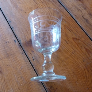 May include: A clear glass goblet with an etched design. The goblet has a round bowl and a tall stem with a round base.