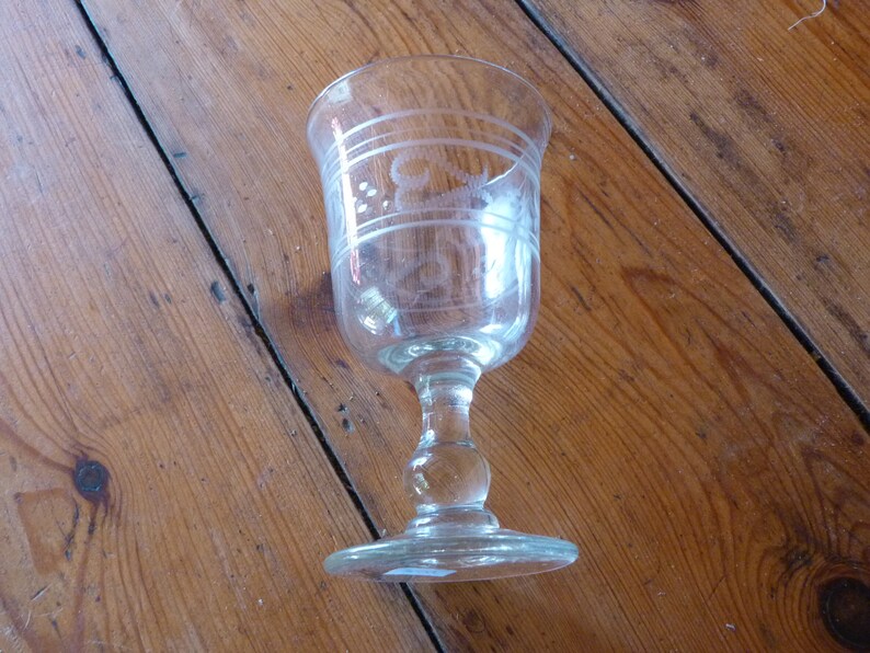 May include: A clear glass goblet with an etched design. The goblet has a round bowl and a tall stem with a round base.