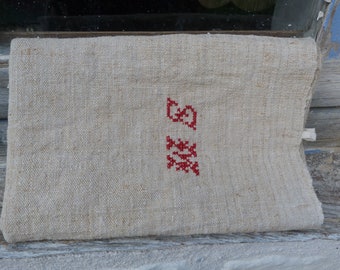 May include: A natural linen fabric pouch with a red embroidered design. The design features a stylized flower with a small square above it.