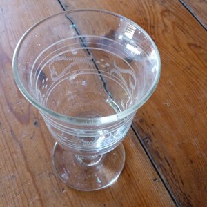 May include: A clear glass goblet with an etched design. The goblet has a round bowl and a stem with a flared base.