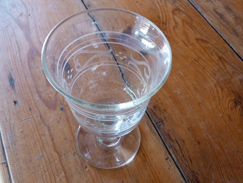 May include: A clear glass goblet with an etched design. The goblet has a round bowl and a stem with a flared base.
