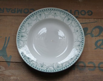 May include: A white ceramic soup bowl with a green floral design around the rim. The bowl is on a wooden surface.