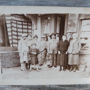 Peut inclure: Photographie vintage en sépia d'un groupe de personnes posant devant un bâtiment. Le groupe comprend des hommes, des femmes et un enfant, tous vêtus de vêtements d'époque. Le bâtiment a un auvent rayé.