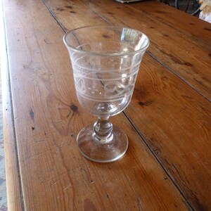 May include: A clear glass goblet with an etched design on the side. The goblet has a round base and a stem.