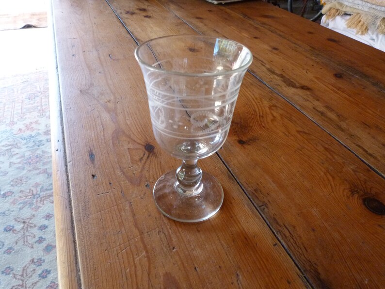 May include: A clear glass goblet with an etched design on the side. The goblet has a round base and a stem.