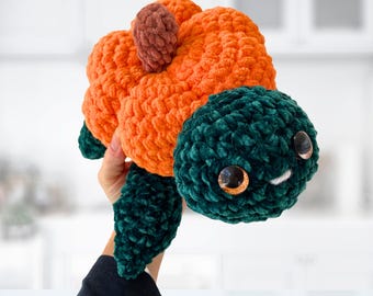 May include: A handmade crochet turtle plushie. The turtle has an orange body, a dark green head and flippers, and a small brown stem. The eyes are large and glittery. The plushie is soft and cuddly.