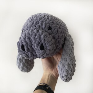 Puede incluir: Un animal de peluche de crochet gris con forma de manat&iacute;. El manat&iacute; tiene un cuerpo peque&ntilde;o y redondo con un hocico largo y delgado y dos peque&ntilde;os ojos negros.