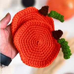 May include: Two crocheted orange pumpkin coasters with green and brown stems.