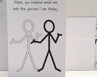 May include: A white greeting card with the text "Mom, you helped mold me into the person I am today..." above a black and white stick figure illustration. A white envelope is visible to the right.