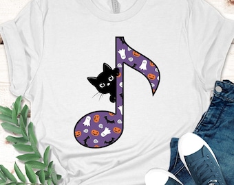 May include: White t-shirt featuring a black cat peeking out from behind a purple musical note. The note is decorated with Halloween-themed patterns, including pumpkins, ghosts, and bats. The shirt is paired with blue jeans and sneakers.