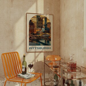K&ouml;nnte beinhalten: Ein Vintage-Poster mit einer Skyline von Pittsburgh, Pennsylvania. Das Poster ist gerahmt und h&auml;ngt an einer Wand in einem Raum mit einem Barwagen und einem Stuhl.