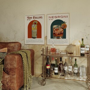 May include: Two vintage-style posters featuring illustrations of classic cocktails. The poster on the left shows a Tom Collins cocktail with the text "Tom Collins Est. 1910". The poster on the right shows a Negroni cocktail with the text "Negroni Est. 1919".