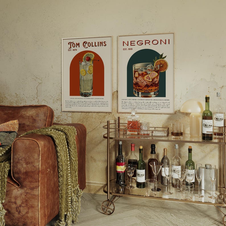 May include: Two vintage-style posters featuring illustrations of classic cocktails. The poster on the left shows a Tom Collins cocktail with the text "Tom Collins Est. 1910". The poster on the right shows a Negroni cocktail with the text "Negroni Est. 1919".