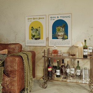 May include: Two vintage-style posters with illustrations of cocktails. The posters are framed and hanging on a wall. The posters are titled "Lemon Basil Smash" and "Gin & Tonic".