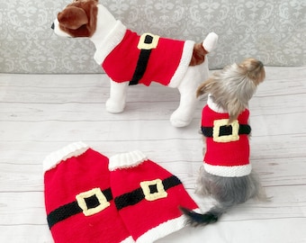 May include: Two dogs wearing red and white knitted Santa Claus sweaters with black belts and yellow buckles. Two additional sweaters are lying on the floor.