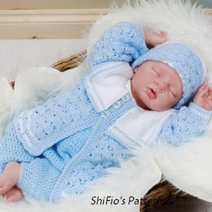 May include: A baby doll wearing a blue and white crocheted outfit with a matching hat. The doll is lying in a white fur-lined basket.