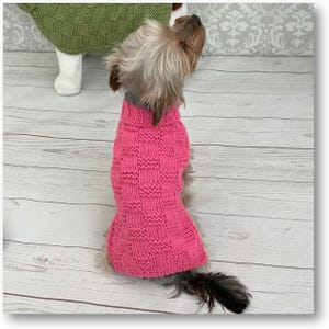 Może przedstawiać: Mały pies w różowym dzianym swetrze. Sweter ma kratkowy wzór.