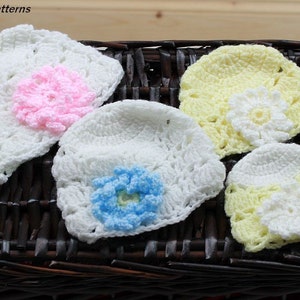 May include: Four crocheted hats with different coloured flowers. The hats are white with a yellow, pink, or blue flower.