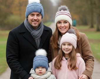 May include: A family of four wearing winter hats and coats. The hats are blue, pink, and cream-colored with white or gray pom-poms. The adults wear black and brown coats, while the children wear a gray jacket and a pink coat. They are standing on a path.