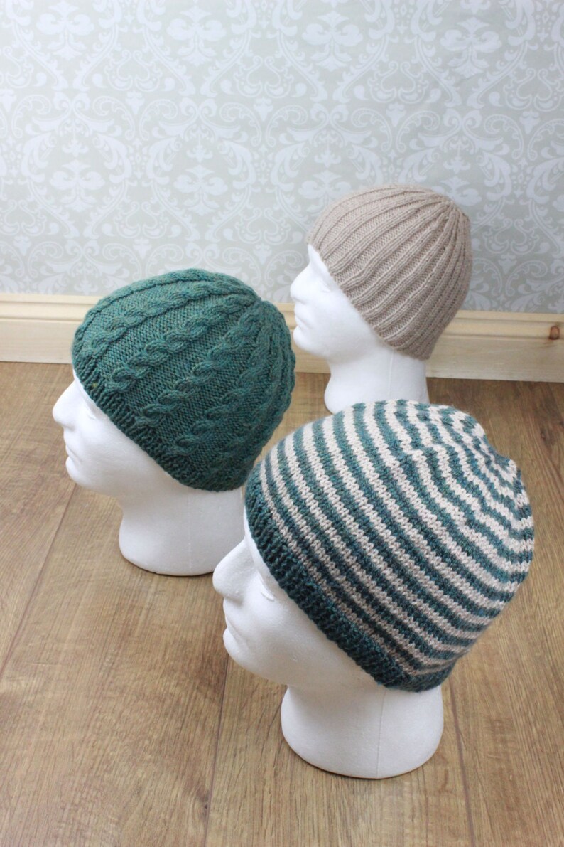 May include: Three knitted hats in different patterns: a green cable knit hat, a striped hat with green and beige stripes, and a beige plain knit hat. The hats are displayed on white mannequin heads.