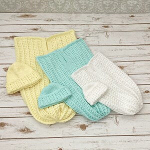 May include: Three crocheted baby sleeping bags in yellow, light blue, and white. Each sleeping bag has a matching crocheted hat.