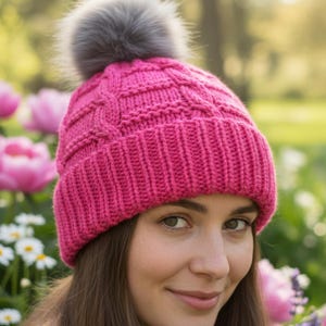 May include: A vibrant pink knitted beanie with a textured pattern and a gray faux fur pom-pom. The hat is designed for warmth and style, perfect for cold weather. The beanie is a fashionable accessory.