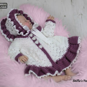 May include: A white and purple crocheted baby jacket and matching bonnet with a white satin ribbon. The jacket has a heart-shaped button closure and a ruffled trim.