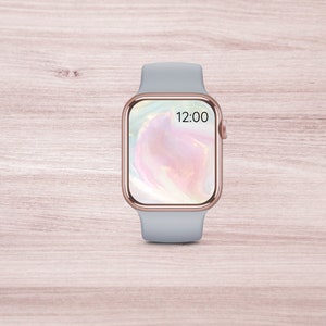 May include: A gray Apple Watch with a rose gold band and a pink and white abstract design on the screen. The time is 12:00.