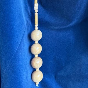 Puede incluir: Una guirnalda de cuentas de madera con una larga hebra de cuentas de madera pequeñas y tres esferas de madera más grandes en la parte inferior. La guirnalda está colgada sobre un fondo de terciopelo azul.