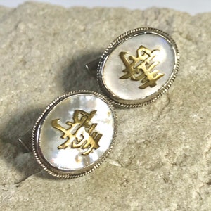May include: A pair of silver cufflinks with a white mother of pearl inlay. The inlay features gold Chinese characters.