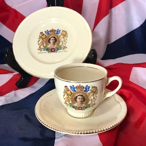 Könnte beinhalten: Cremefarbenes Tee-Set bestehend aus Tasse, Untertasse und Teller. Jedes Teil zeigt ein Porträt einer Frau mit Krone und dem Text "Coronation June 2nd 1953". Das Set hat einen Goldrand und einen geriffelten Rand.
