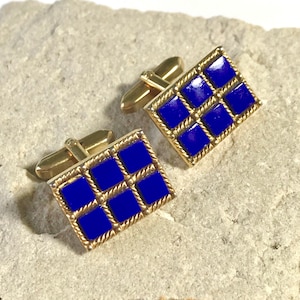 Könnte beinhalten: Ein Paar goldene Manschettenknöpfe mit einem blauen Emaille-Design. Die Manschettenknöpfe sind rechteckig und haben ein Gittermuster aus neun Quadraten.