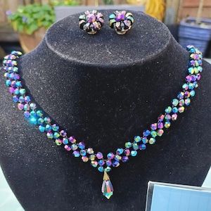 May include: A black choker necklace with a teardrop pendant made of iridescent glass beads. The necklace is paired with a set of matching iridescent glass earrings.
