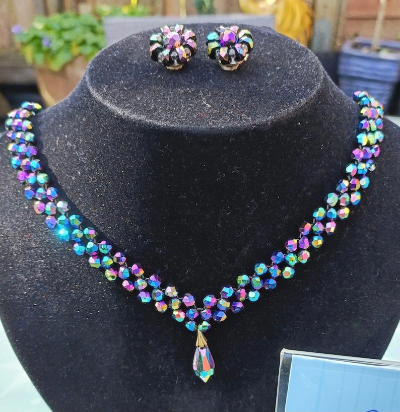 May include: A black choker necklace with a teardrop pendant made of iridescent glass beads. The necklace is paired with a set of matching iridescent glass earrings.