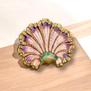 Könnte beinhalten: Eine dekorative Schale in Muschelform mit einer rosa und violetten Emaille-Oberfläche. Die Schale hat einen goldfarbenen Rand und aufwendige Details.