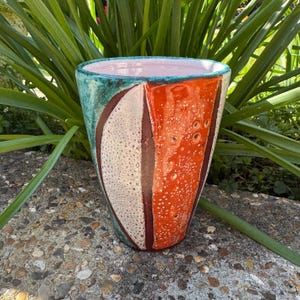 May include: A ceramic vase with a geometric design in shades of orange, white, brown, and teal.