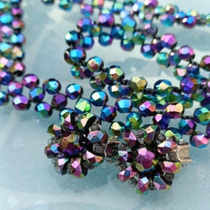 May include: A multi-strand necklace made of iridescent black faceted beads. The necklace has a clasp made of silver metal.