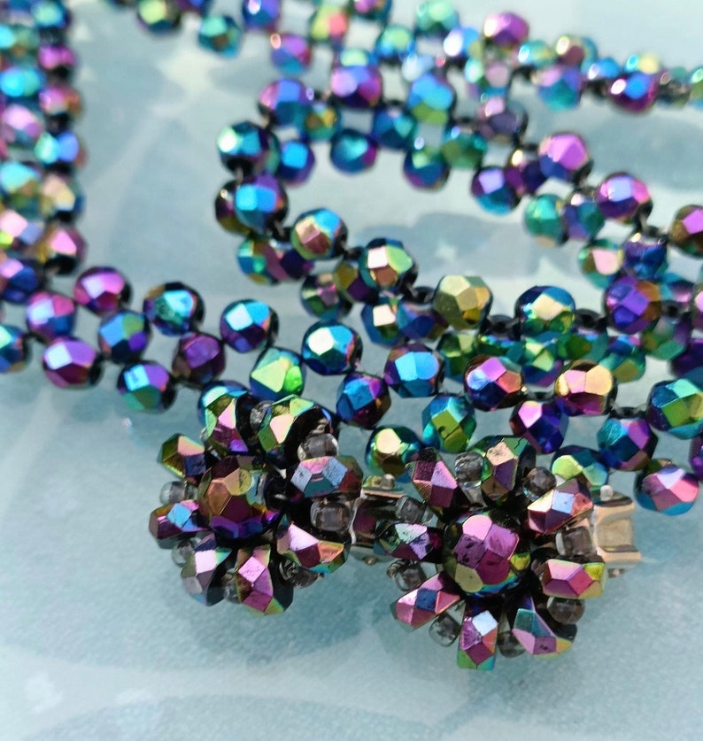 May include: A multi-strand necklace made of iridescent black faceted beads. The necklace has a clasp made of silver metal.