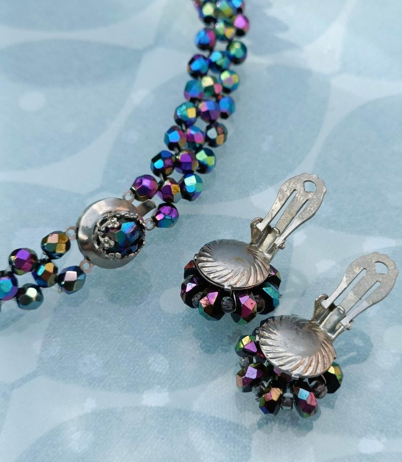 May include: A set of iridescent purple and blue glass bead jewelry, including a necklace and a pair of clip-on earrings. The necklace has a silver clasp and the earrings have silver backs.