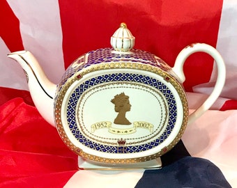 May include: White teapot with a blue and gold design. The teapot features a portrait of Queen Elizabeth II and the years 1952 and 2002.