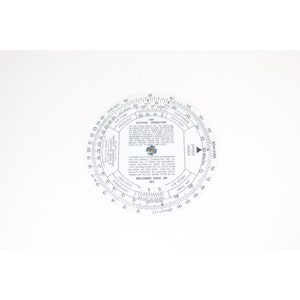 May include: A white circular slide rule with black markings for air speed and altitude correction. The slide rule has a central dial with a speed index and a rotating outer dial with scales for altitude, air temperature, and pressure altitude.