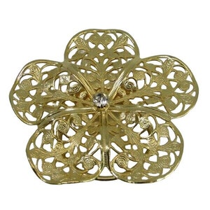 Può includere: Un fermaglio a forma di fiore in metallo dorato con un brillante di strass trasparente al centro. Il fiore ha un design delicato e intricato.