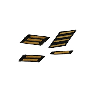 May include: Four black and gold embroidered patches, likely military or uniform insignia, are displayed against a white background. The patches feature gold stripes on a black base, with varying numbers of stripes indicating rank or status.